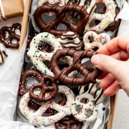 hand grabbing chocolate covered pretzel from lined box.