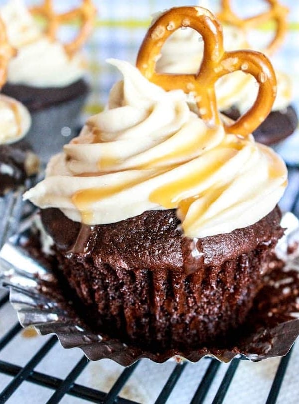chocolate cupcakes topped with salted caramel frosting and a pretzel on a cooling rack