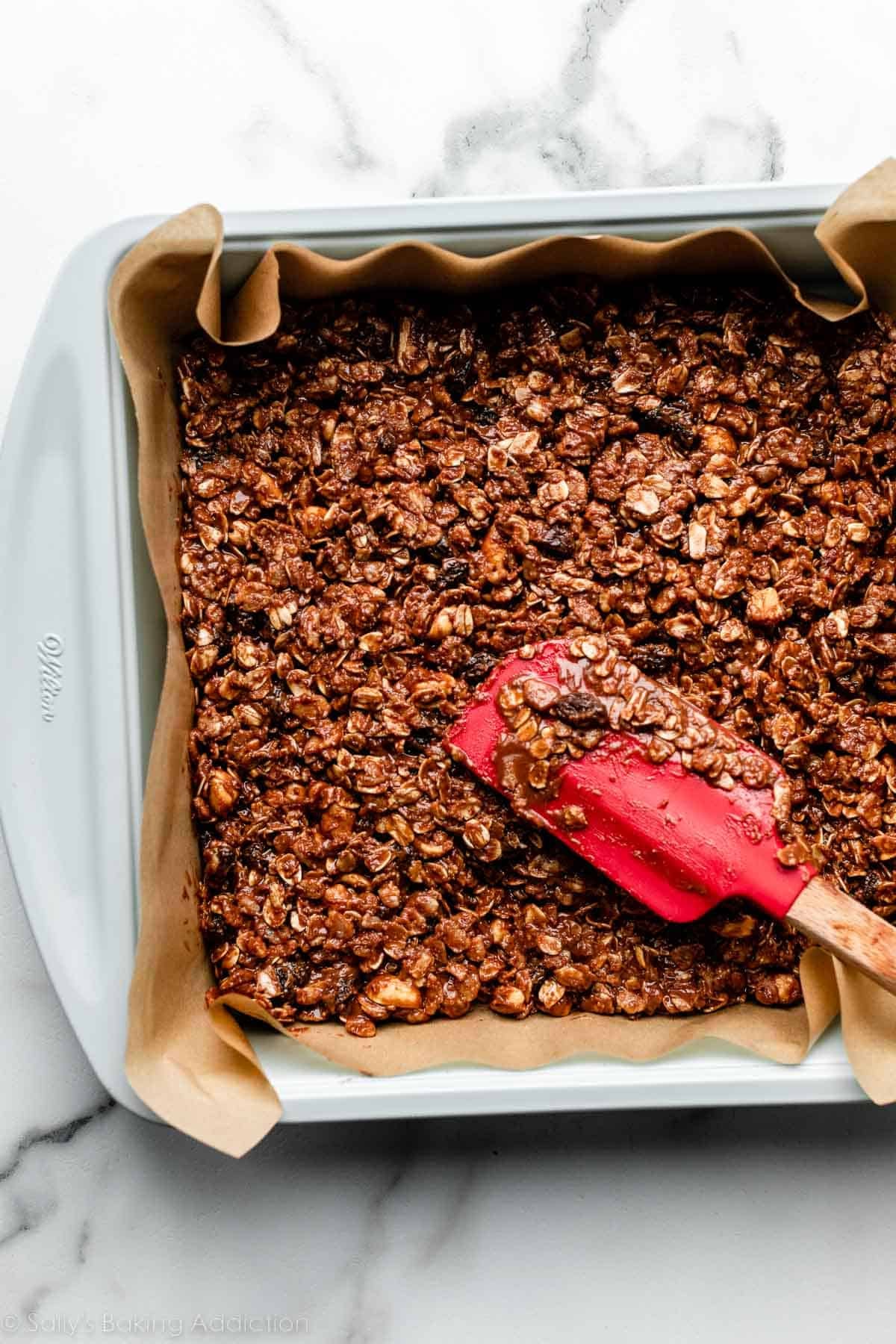 red spatula smoothing chocolate oat mixture into parchment paper-lined baking pan.