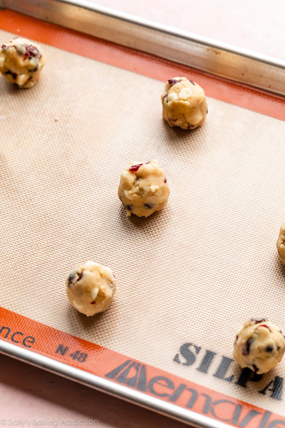 white chocolate chip cranberry cookie dough balls on lined baking sheet