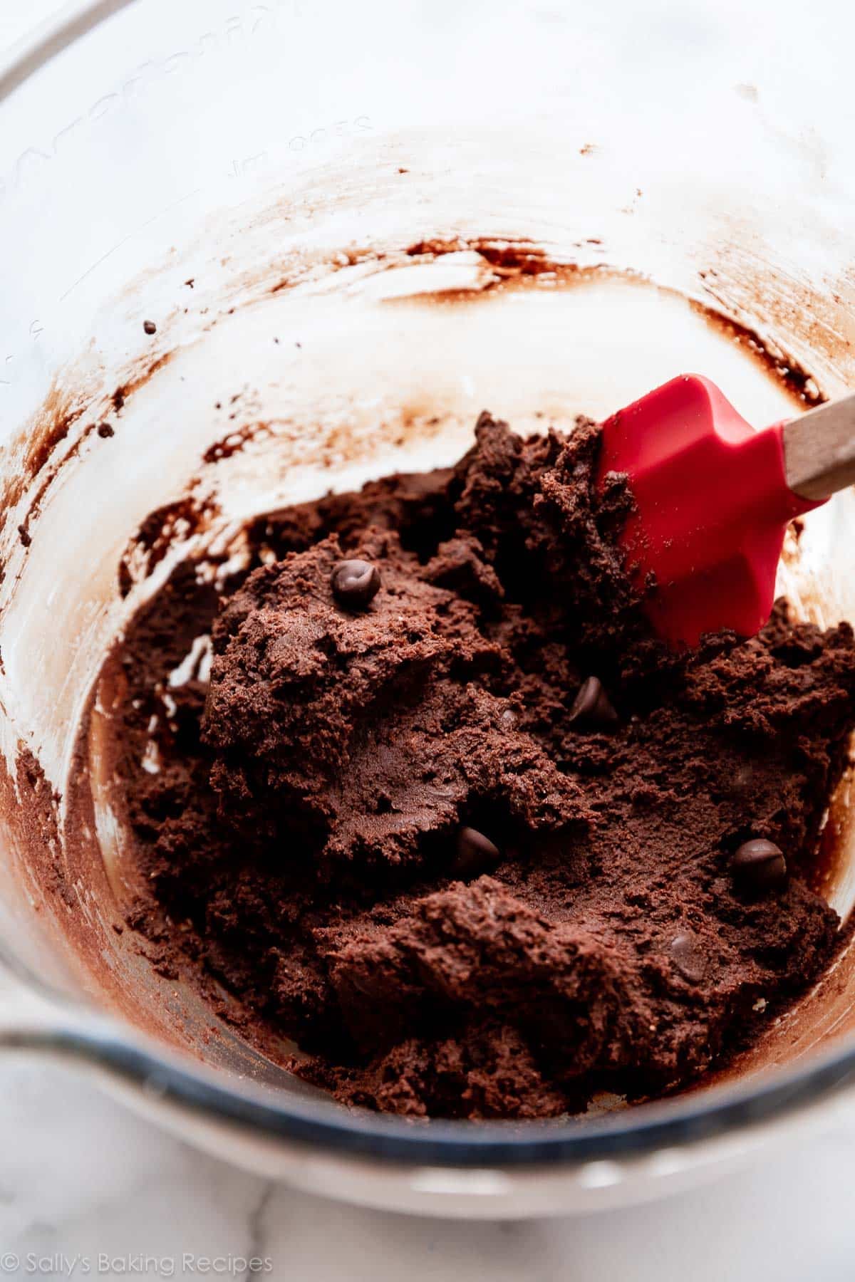 chocolate cookie dough with red spatula in glass mixing bowl.