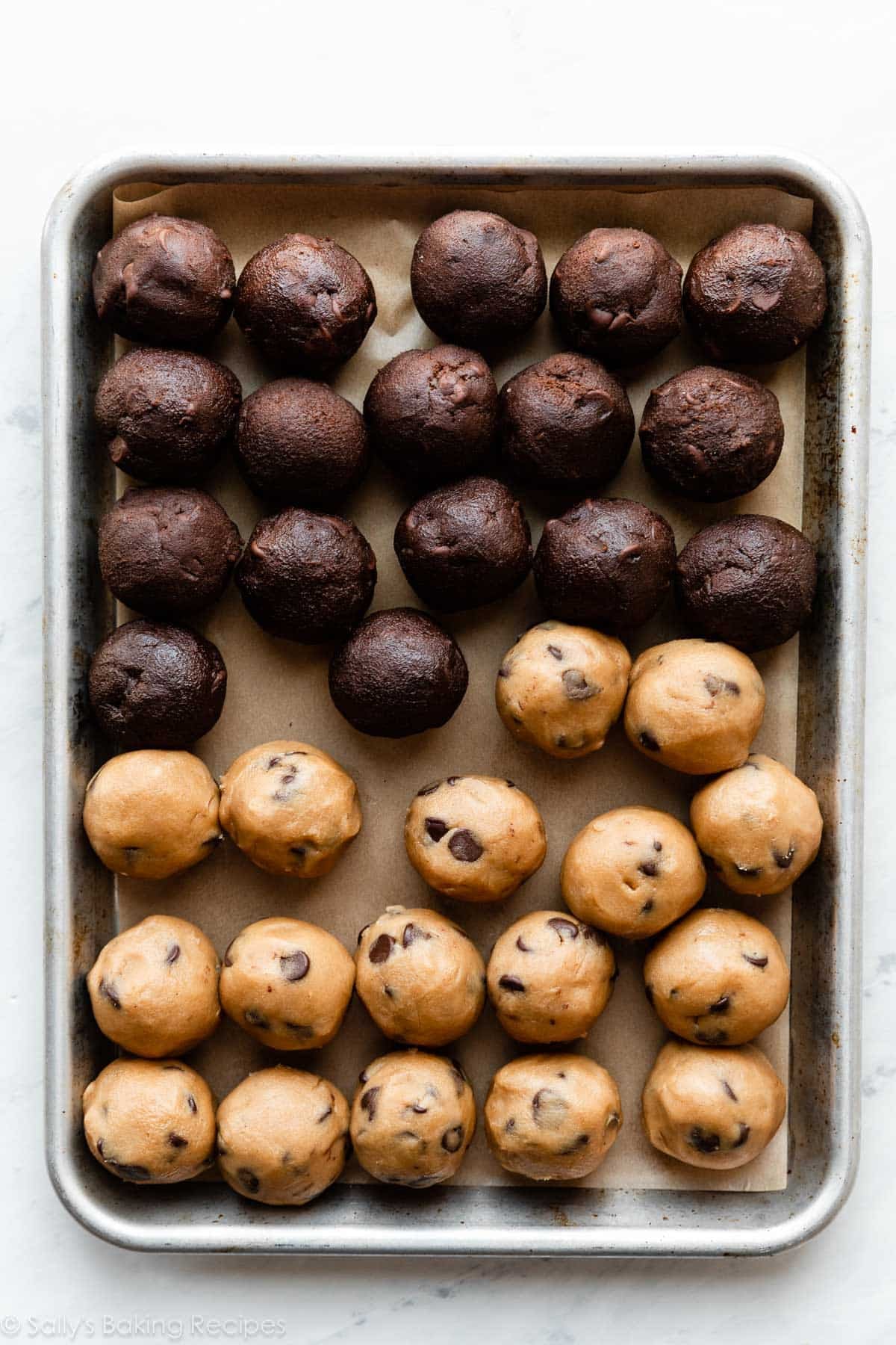 lined baking sheet with chocolate cookie dough balls and peanut butter cookie dough balls on top.