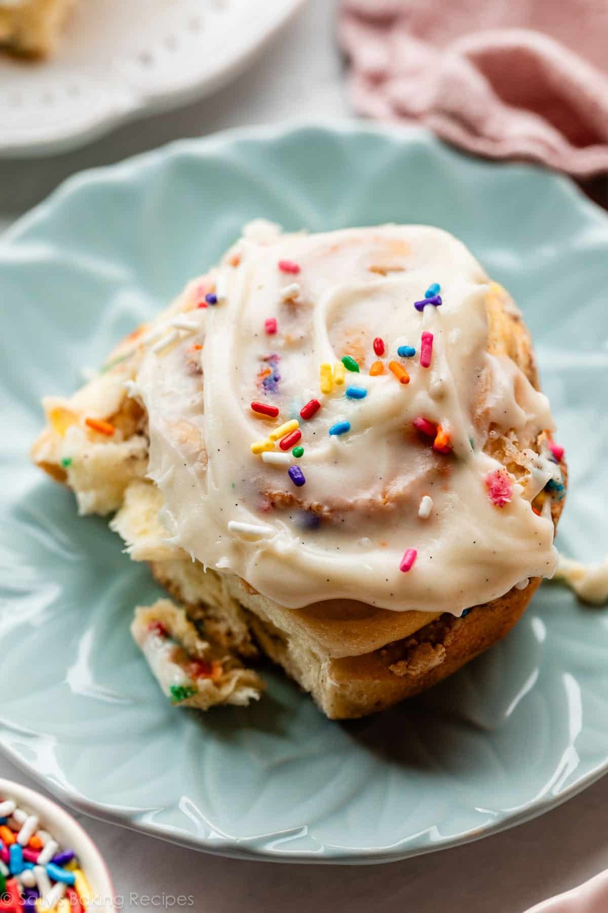 birthday cake cinnamon roll with sprinkles on top on blue plate.