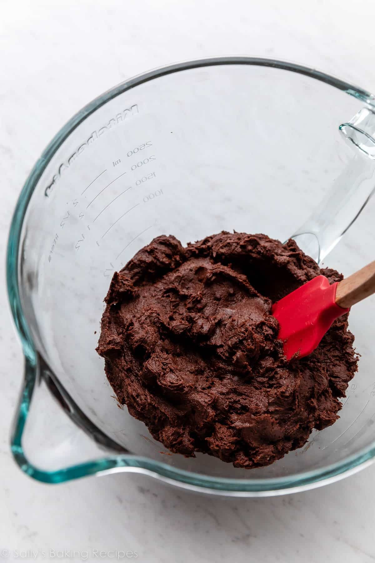 chocolate cookie dough in glass bowl with red spatula.