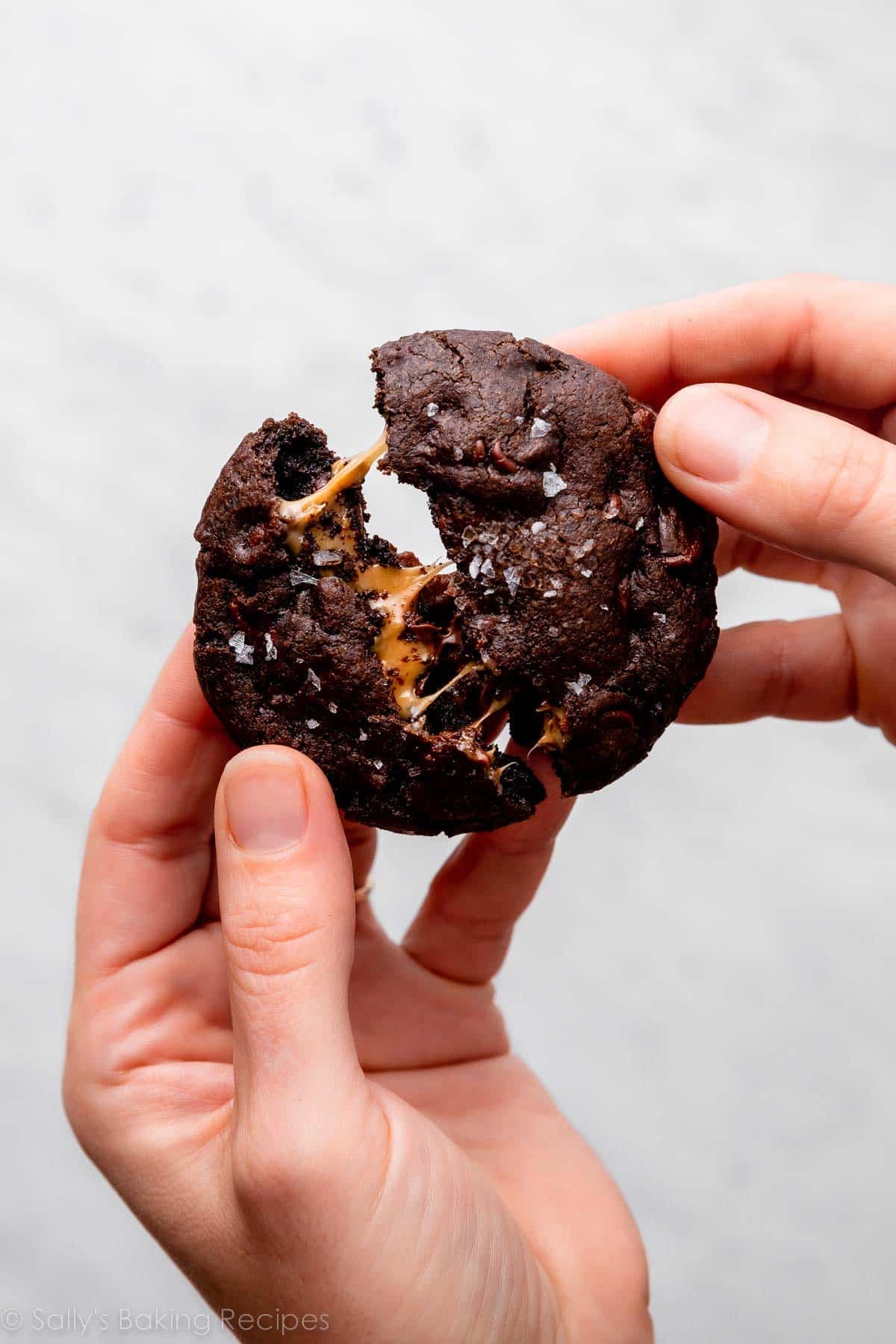 hands breaking apart a chocolate cookie with caramel center.
