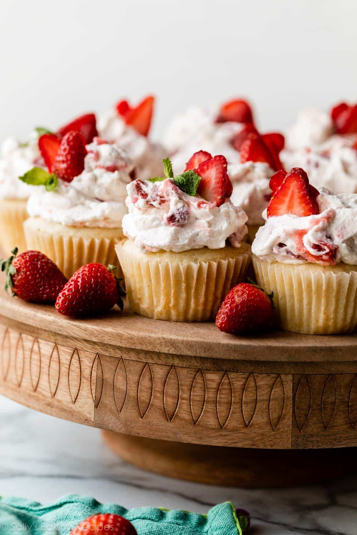 strawberry shortcake cupcakes with strawberry whipped cream arranged on wooden cake stand.