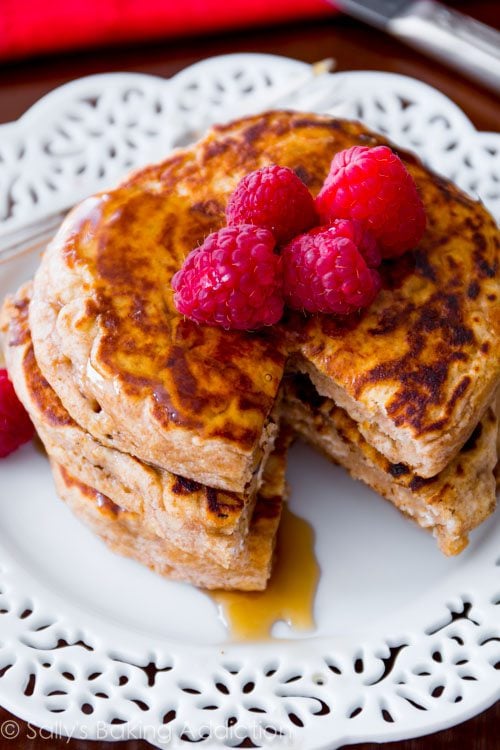 stack of whole wheat oatmeal pancakes topped with raspberries and maple syrup on a white plate