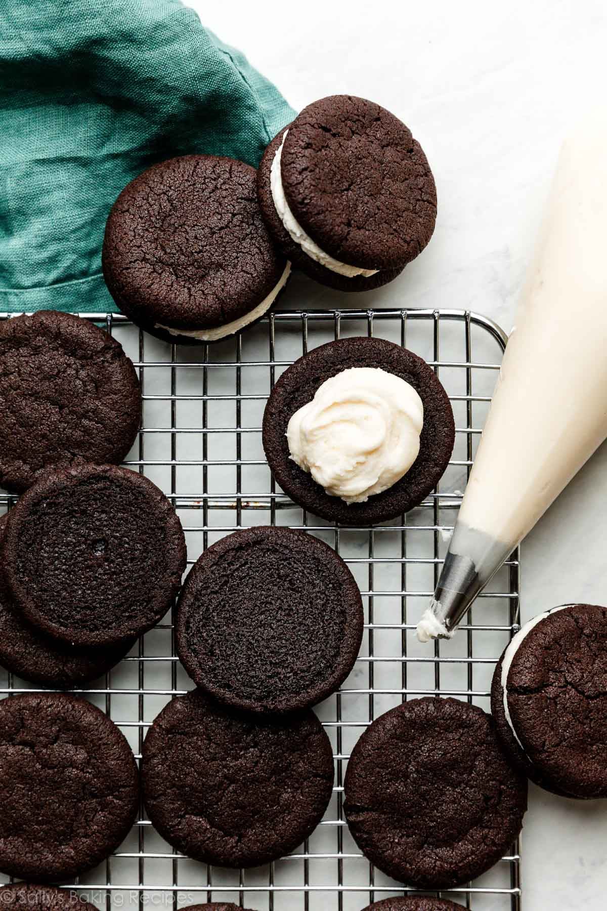 chocolate cookies on cooling rack with piping bag next to it and one cookie with cream piped on top.