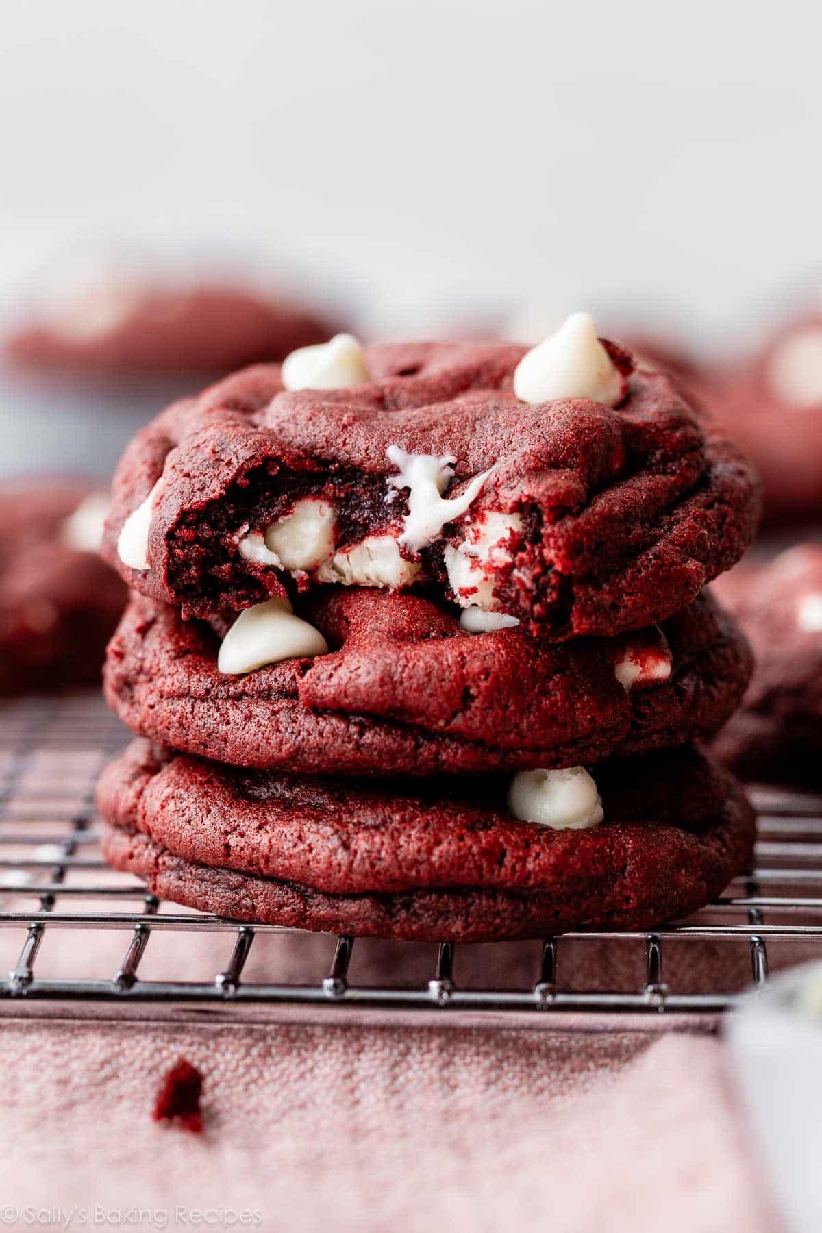 stack of red velvet white chocolate chip cookies on a cooling rack.