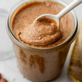 homemade almond butter in jar with white spoon.