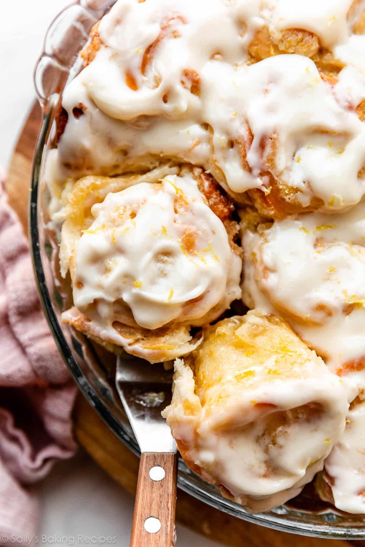 spatula removing a lemon sweet roll with cream cheese icing from the pan.