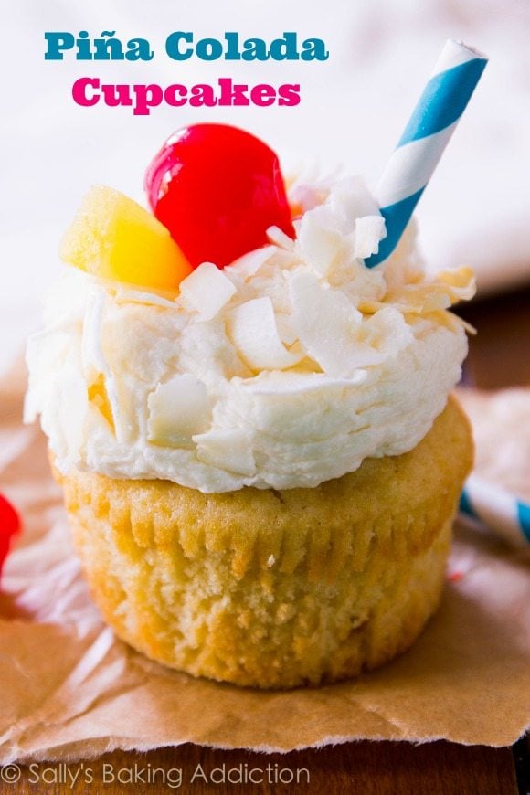 piña colada cupcakes topped with coconut frosting, shredded coconut, a cherry, slice of pineapple, and a straw