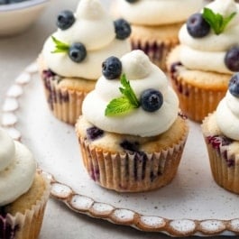 blueberry cupcakes with whipped cream cheese frosting on top with fresh mint.