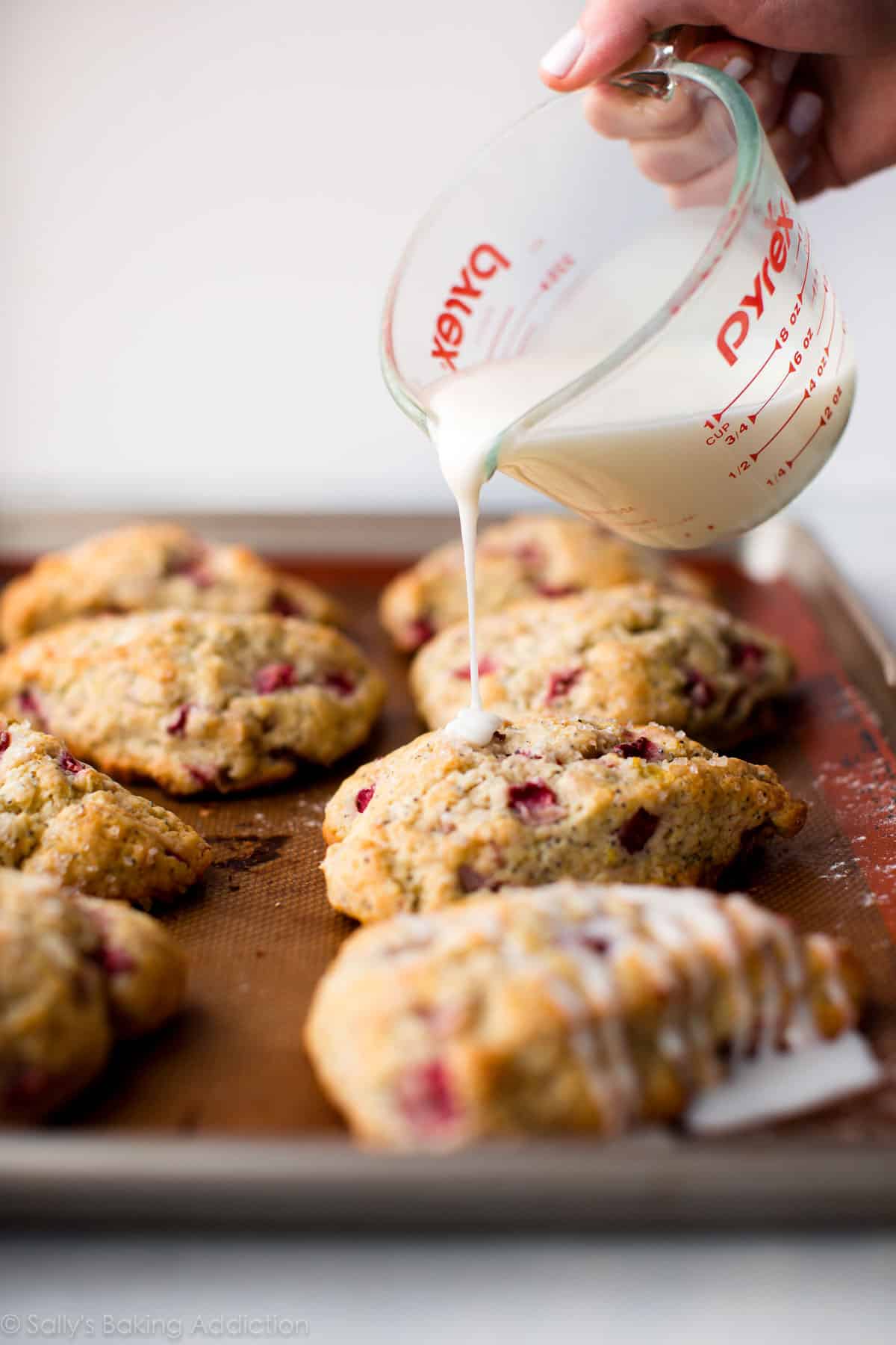 pouring lemon icing on top of strawberry scones