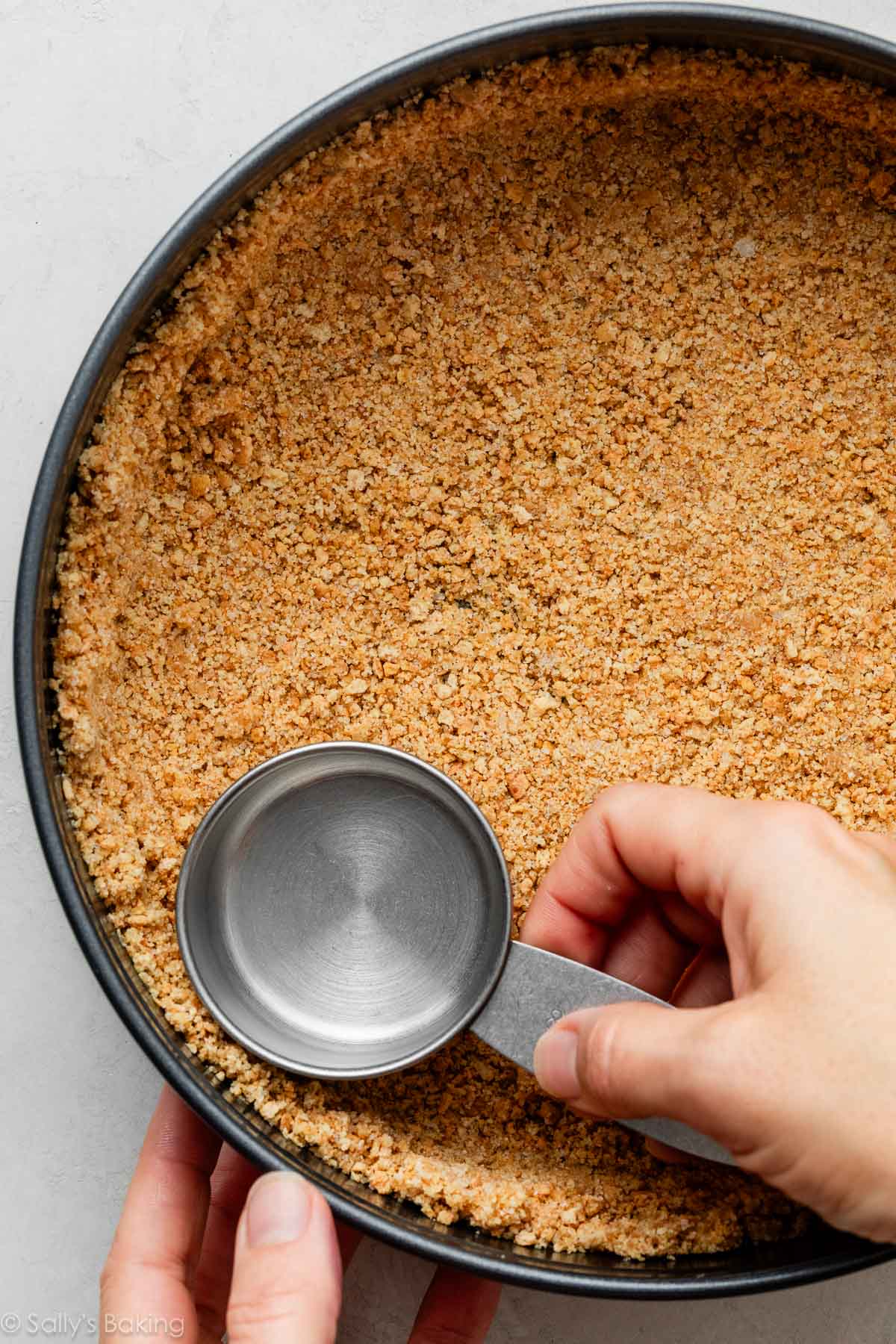 hands pressing graham cracker crust into springform pan.