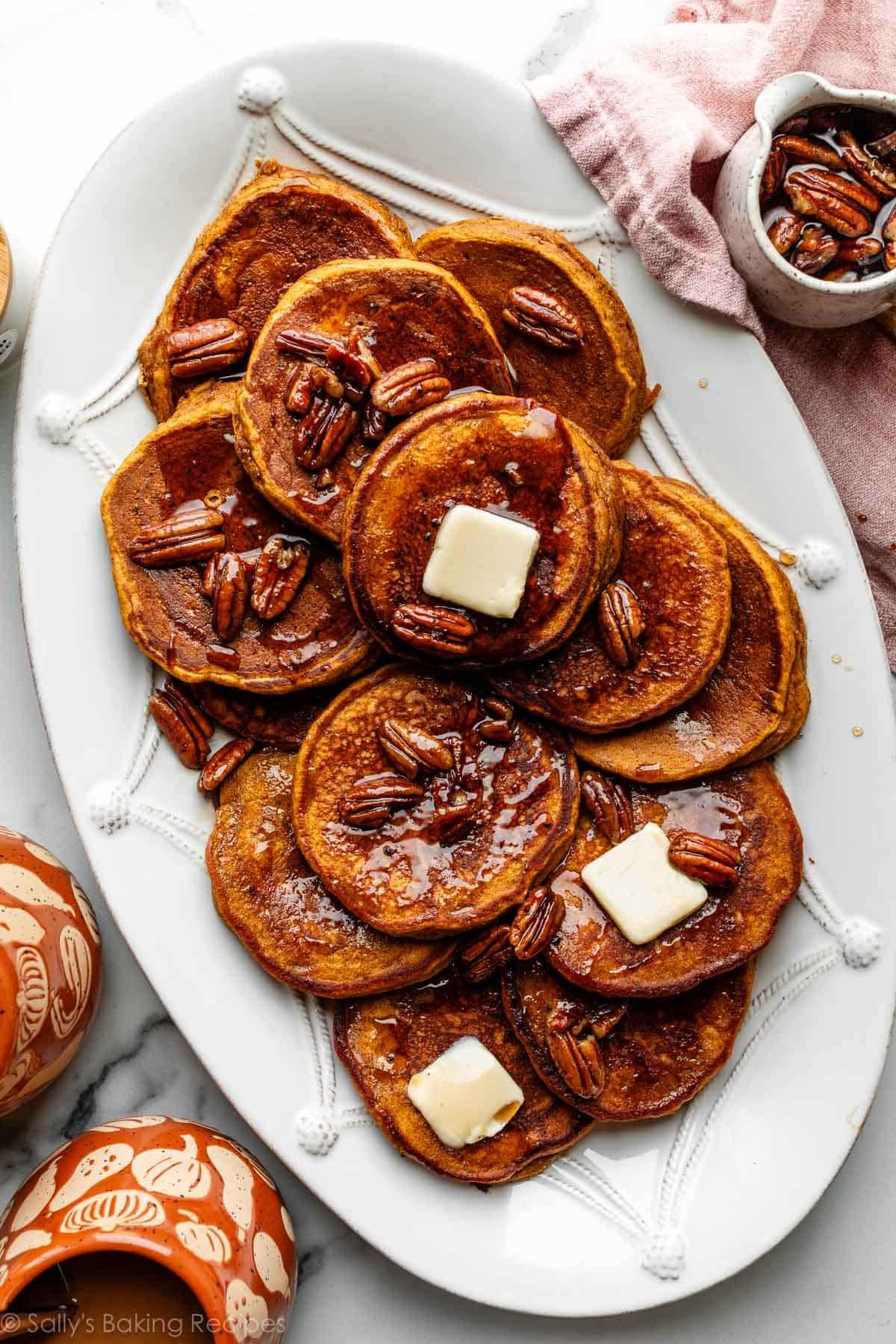 pumpkin pancakes with slices of butter and maple pecan syrup on top sitting on white platter.