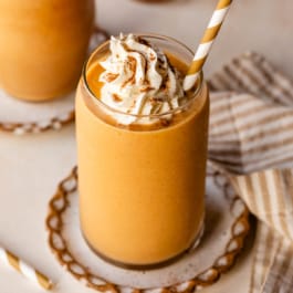 pumpkin pie smoothie in glass cup with whipped cream and striped straw.