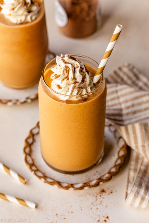 pumpkin pie smoothie in glass cup with whipped cream and striped straw.