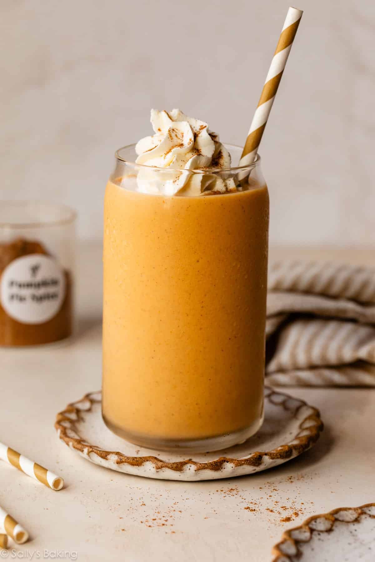 pumpkin pie smoothie in glass cup with whipped cream and striped straw.