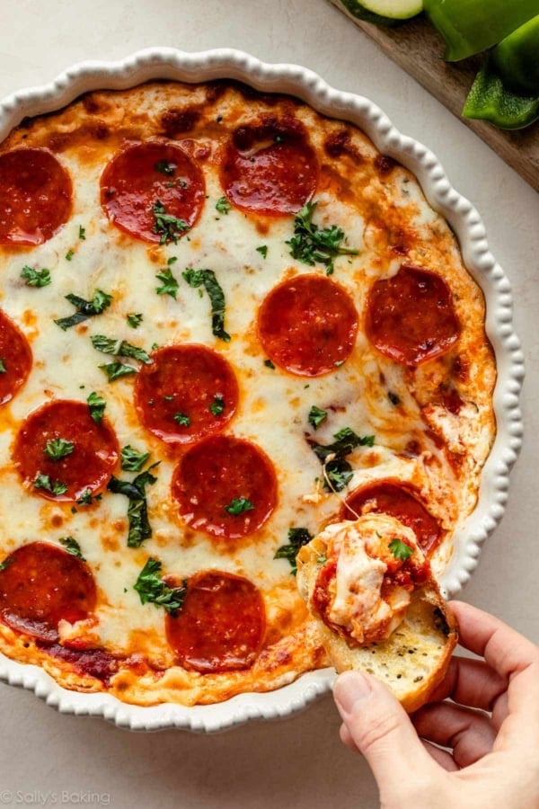 crostini being dipped in pizza dip with pepperonis on top.