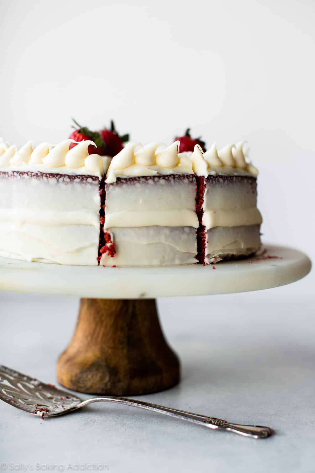 sliced red velvet layer cake on a marble and wood cake stand
