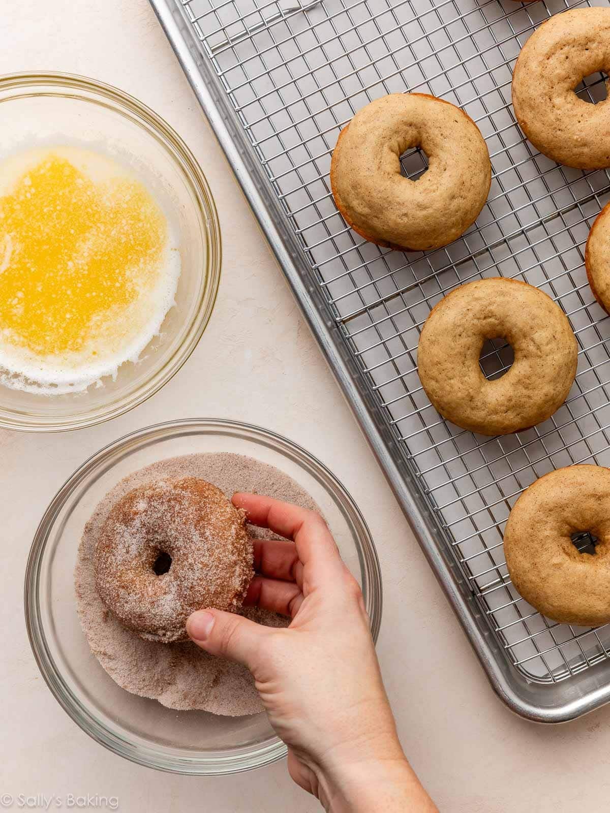hands coating donuts in sugar.