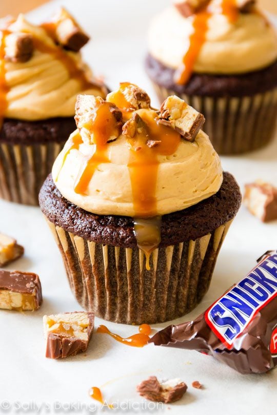 chocolate cupcakes topped with peanut butter frosting, chopped Snickers candy bars, and salted caramel