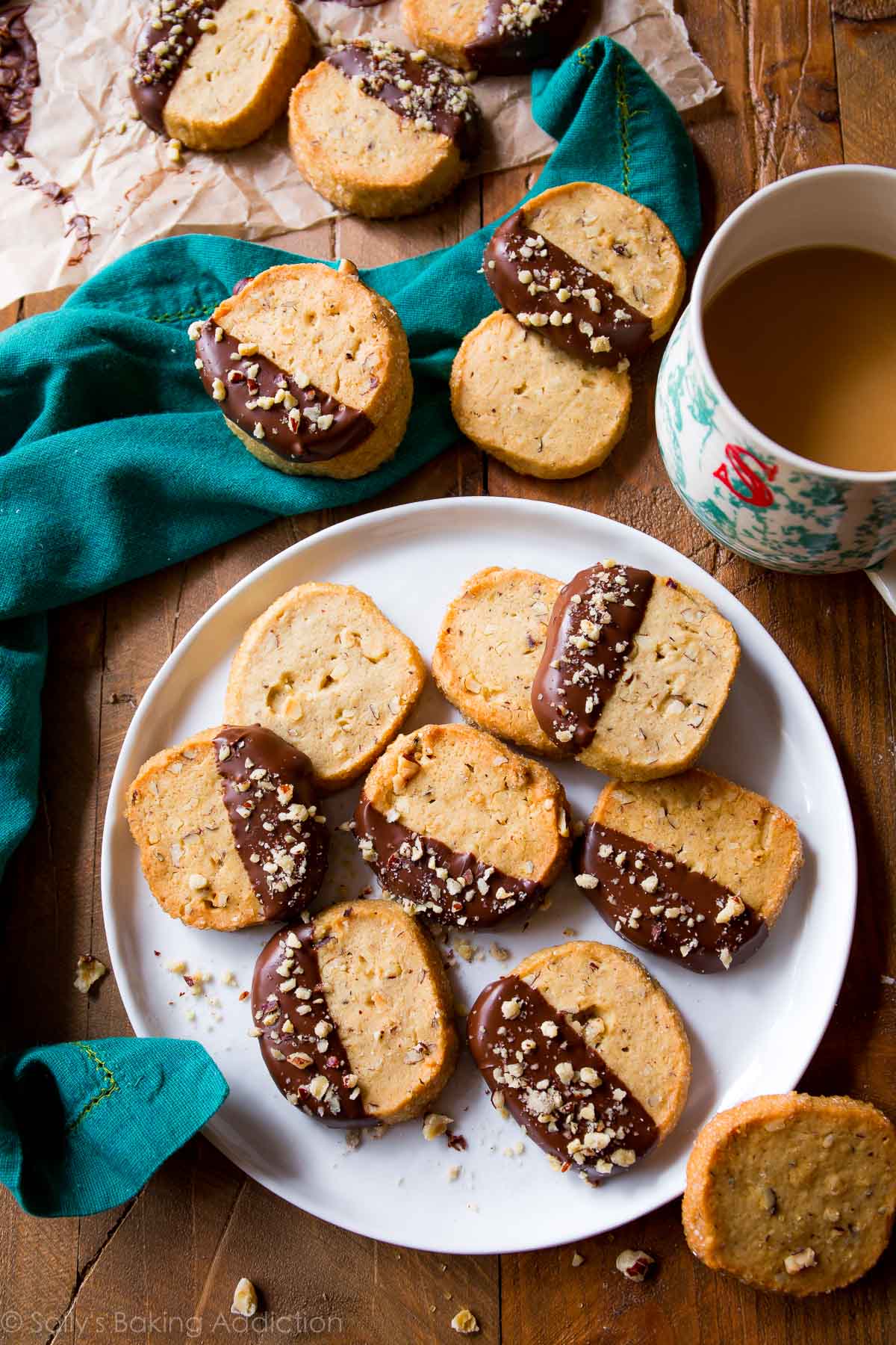 overhead image of toasted hazelnut slice and bake cookies with half of each cookie dipped in milk chocolate on a white plate with a cup of coffee