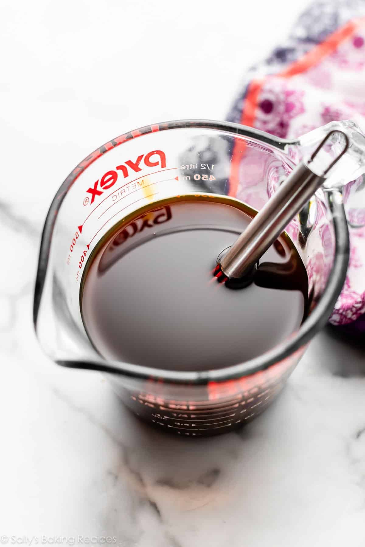 molasses water mixture in liquid measuring cup with purple linen in background.
