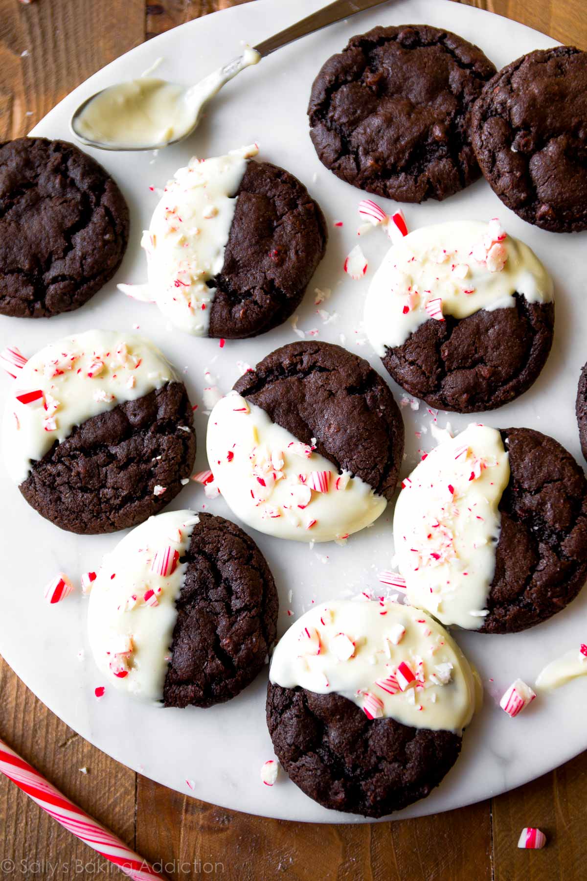 overhead image of peppermint mocha cookies with half of each cookie dipped in white chocolate and topped with crushed candy canes on a marble serving tray