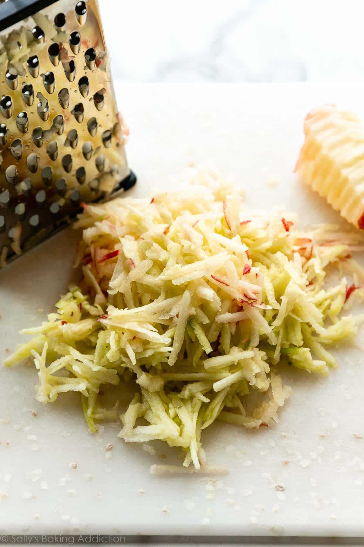 shredded red and green apple on white cutting board.