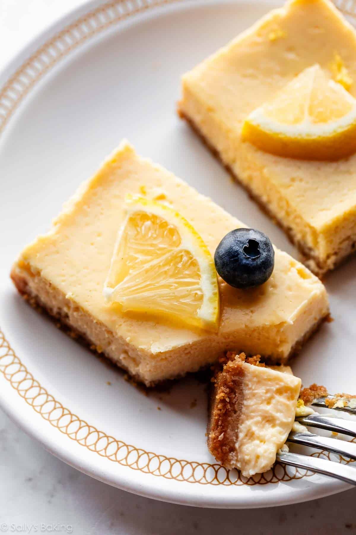 Greek yogurt lemon bars on graham cracker crust with fresh lemon and blueberry on top.