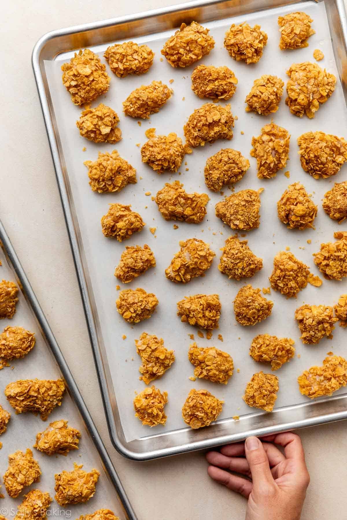 hand taking tray of coated chicken pieces away.
