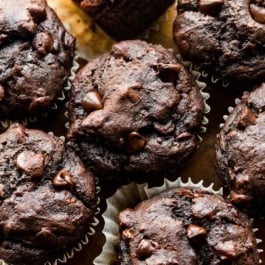 up close photo showing the tops of chocolate banana muffins on a wooden cutting board.
