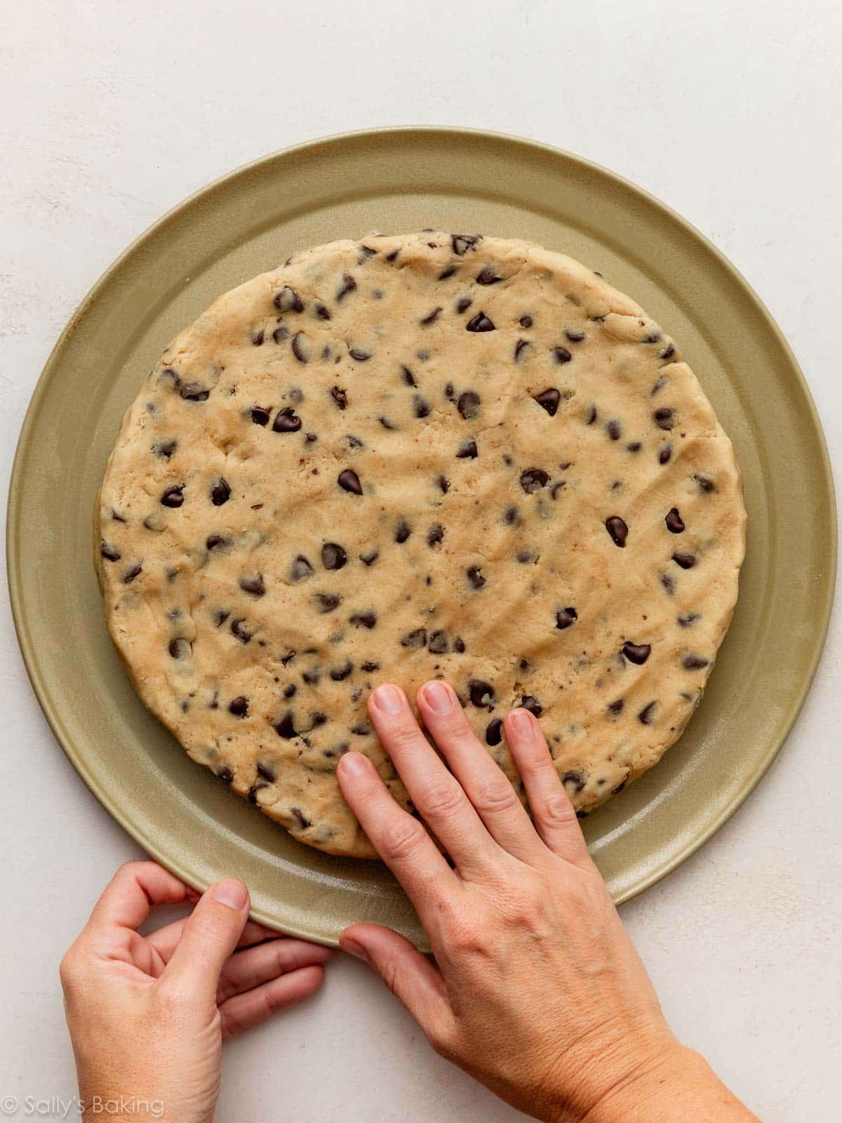 hands flattening cookie dough on gold pizza pan.