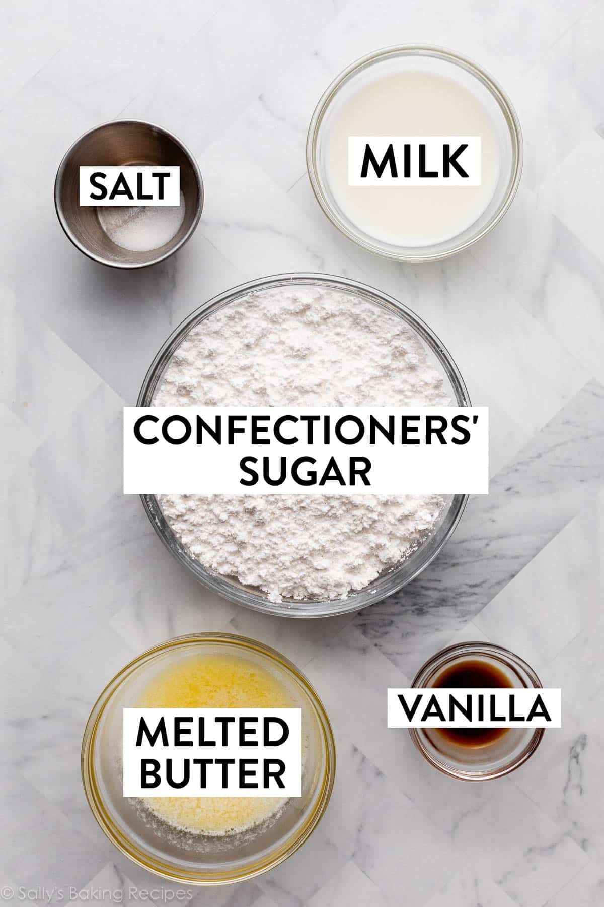 ingredients on marble counter including confectioners' sugar, milk, salt, vanilla, and melted butter.