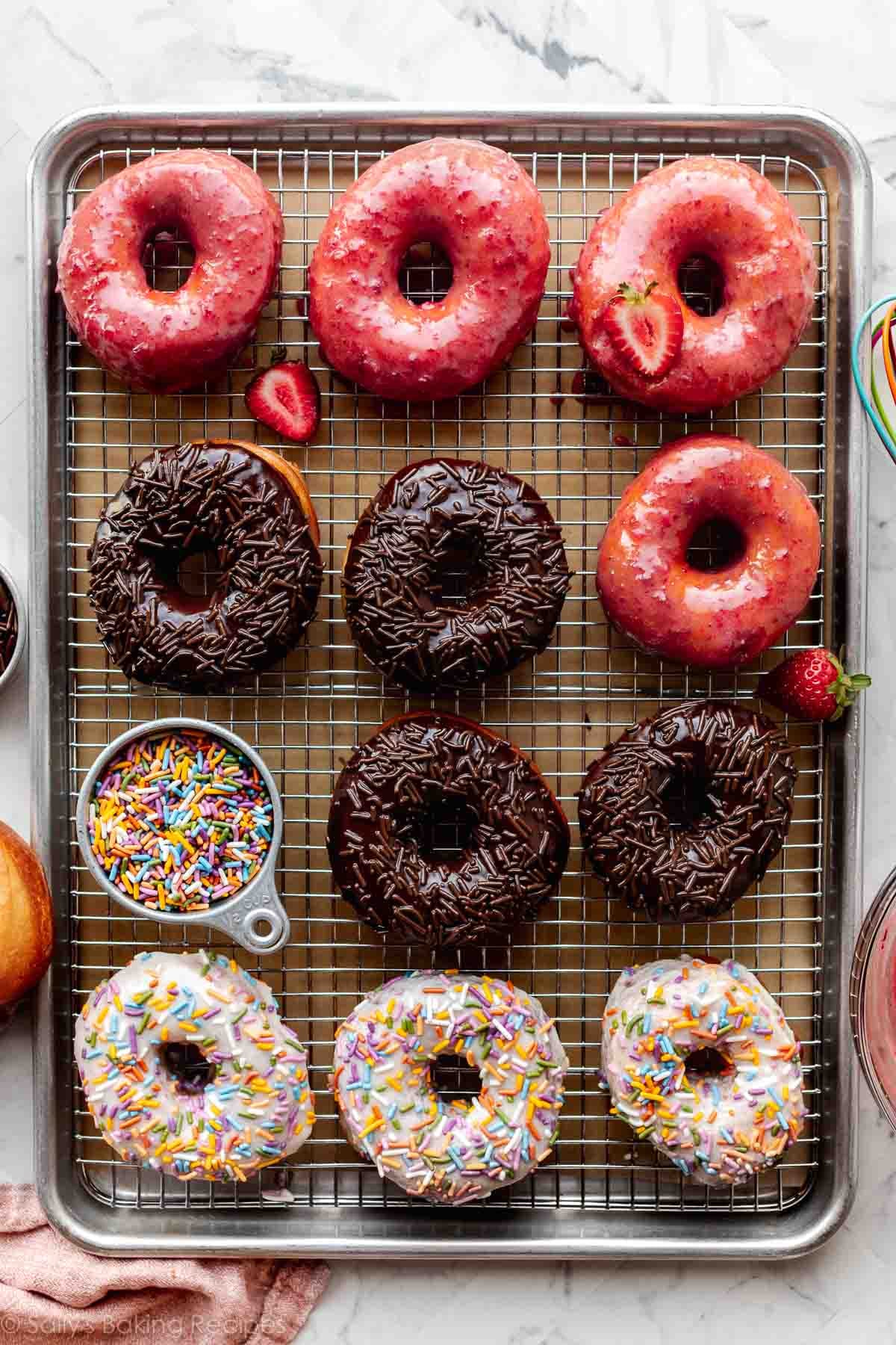 strawberry, chocolate, and vanilla frosted doughnuts on wire cooling rack on top of baking sheet pan.