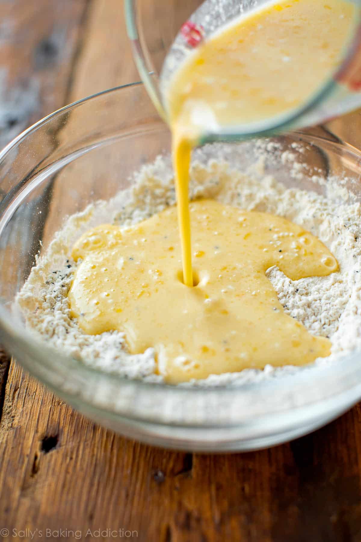 pouring wet ingredients into a glass bowl full of dry ingredients