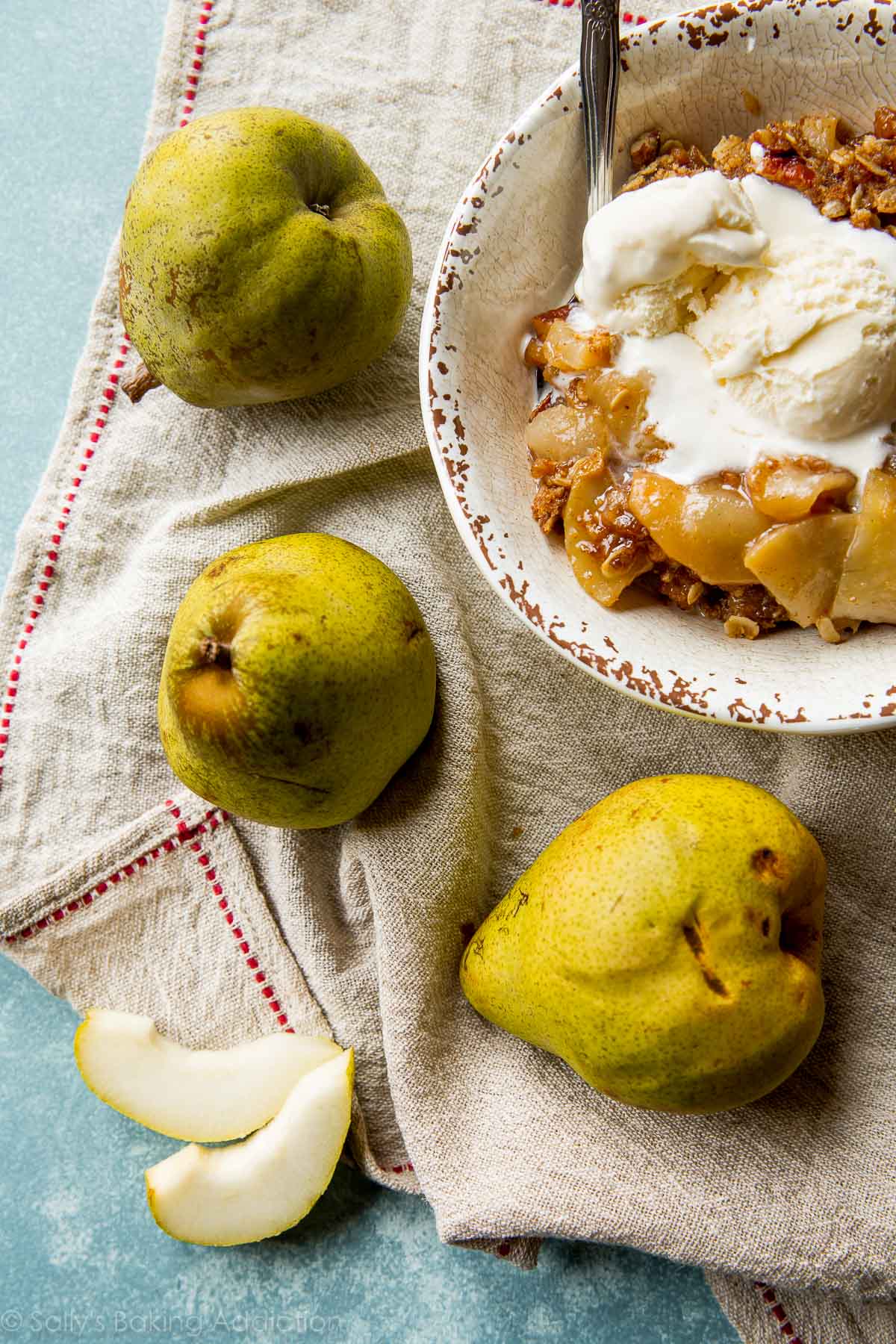 overhead image of a serving of apple pear crisp in a white bowl with a spoon and vanilla ice cream