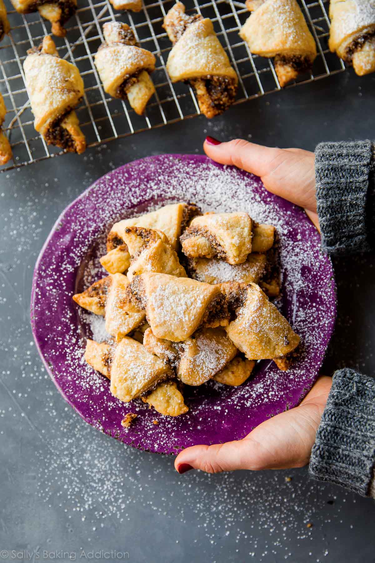 hands holding a purple plate of rugelach cookies