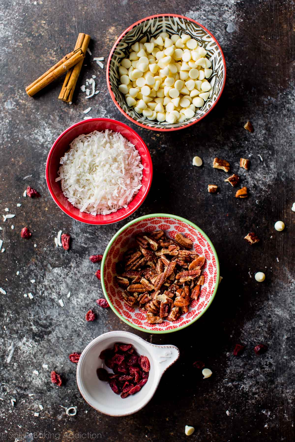 overhead image of bowls of white chocolate chips, shredded coconut, pecans, and dried cranberries
