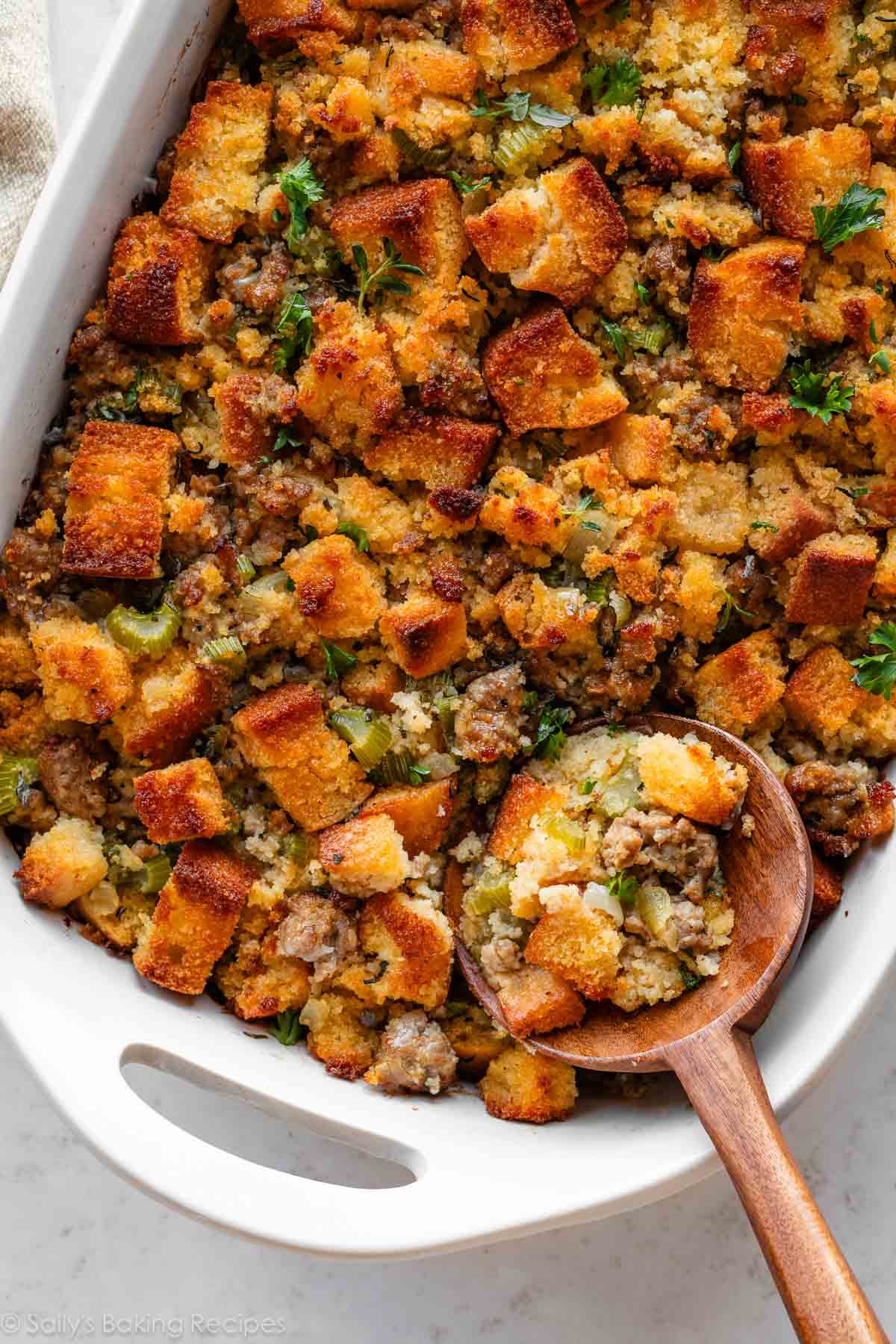 wooden spoon scooping out cornbread stuffing from white dish.