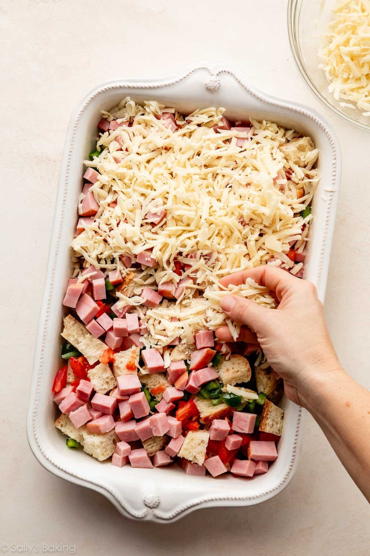 sprinkling cheese on cubed bread and ham.