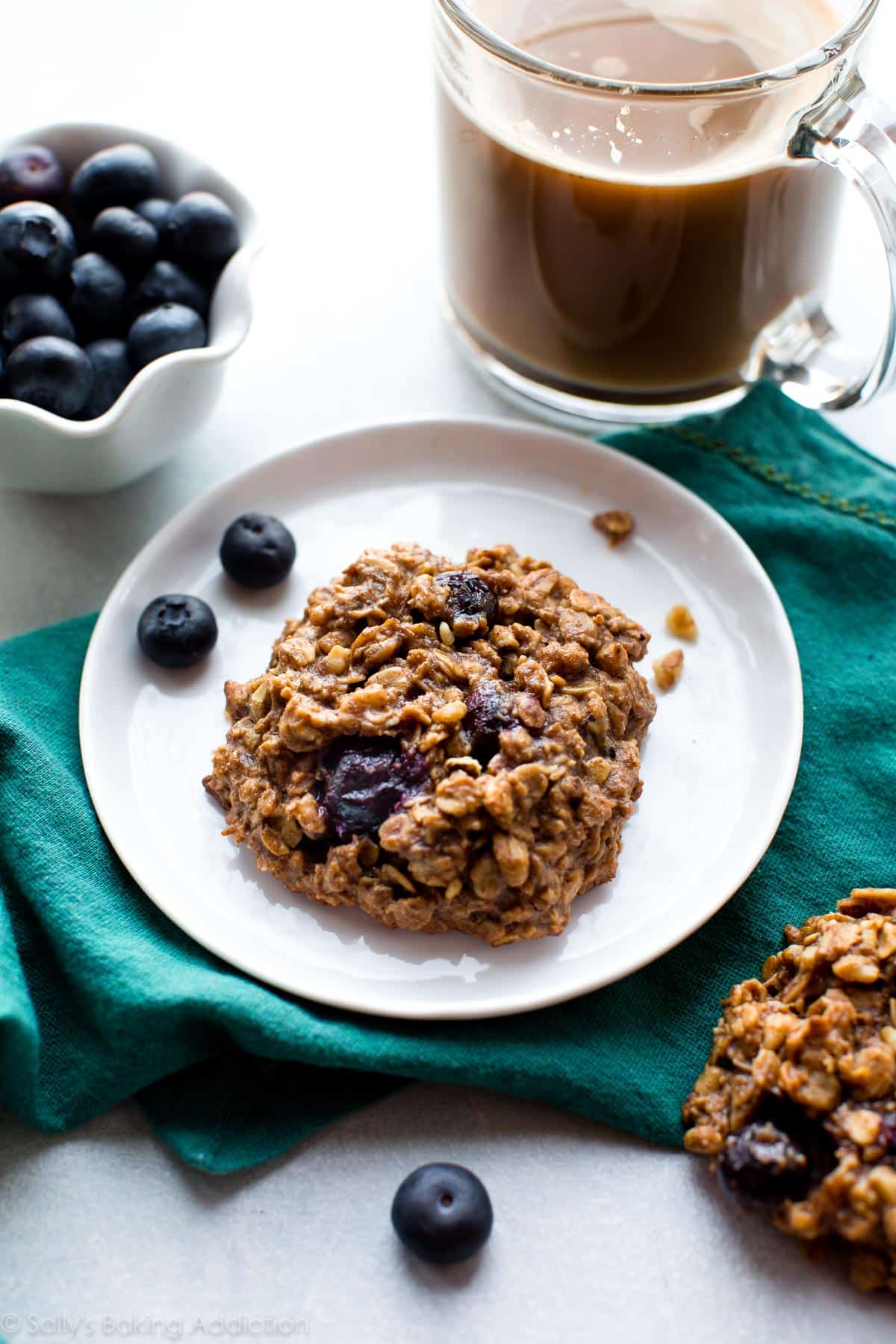 blueberry breakfast cookie on a white plate with a cup of coffee