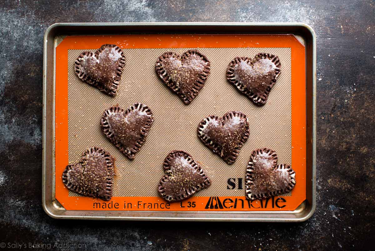 overhead image of heart shaped chocolate hand pies on a baking sheet lined with a silpat baking mat before baking