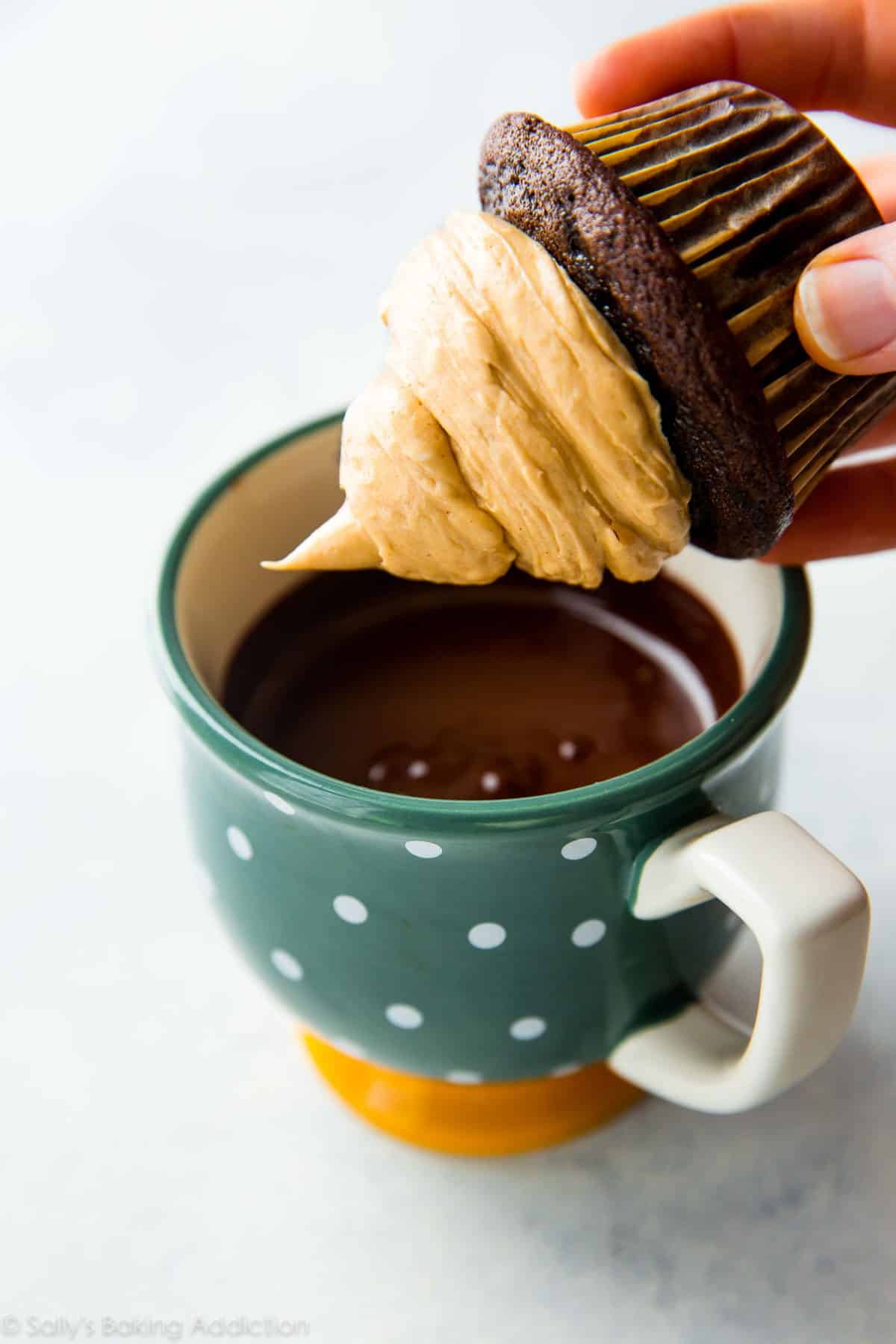 hands dunking a chocolate cupcake with peanut butter frosting into a mug of chocolate coating