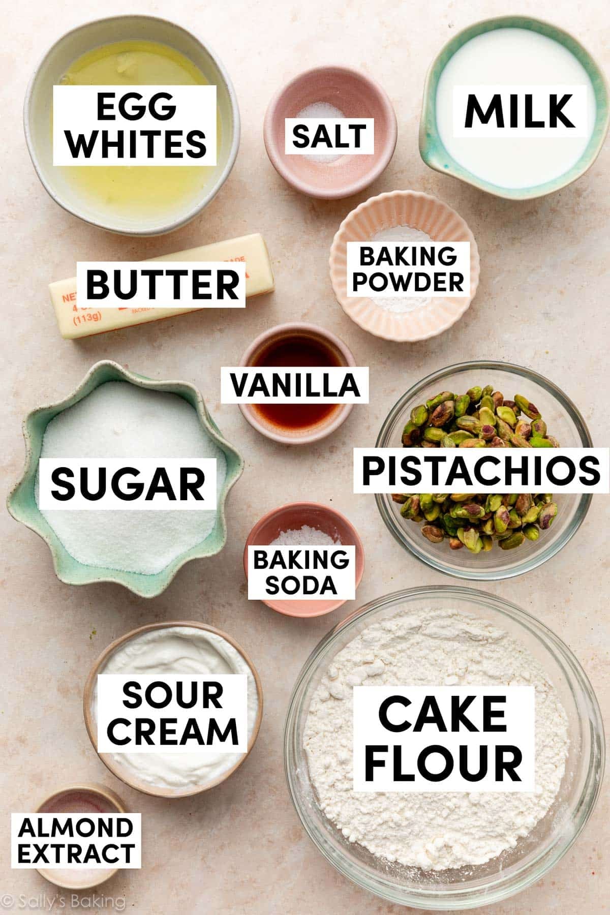 ingredients on peach surface including cake flour, sour cream, milk, egg whites, butter, sugar, almond extract, and vanilla.