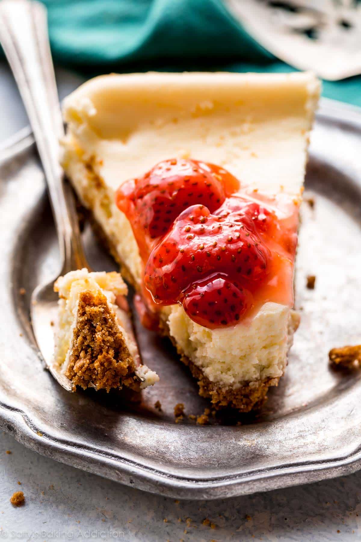 slice of cheesecake with strawberry topping on a silver plate with a fork