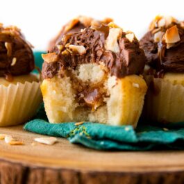 chocolate caramel coconut cupcakes on a wood slice serving board with a bite out of one showing the caramel filling