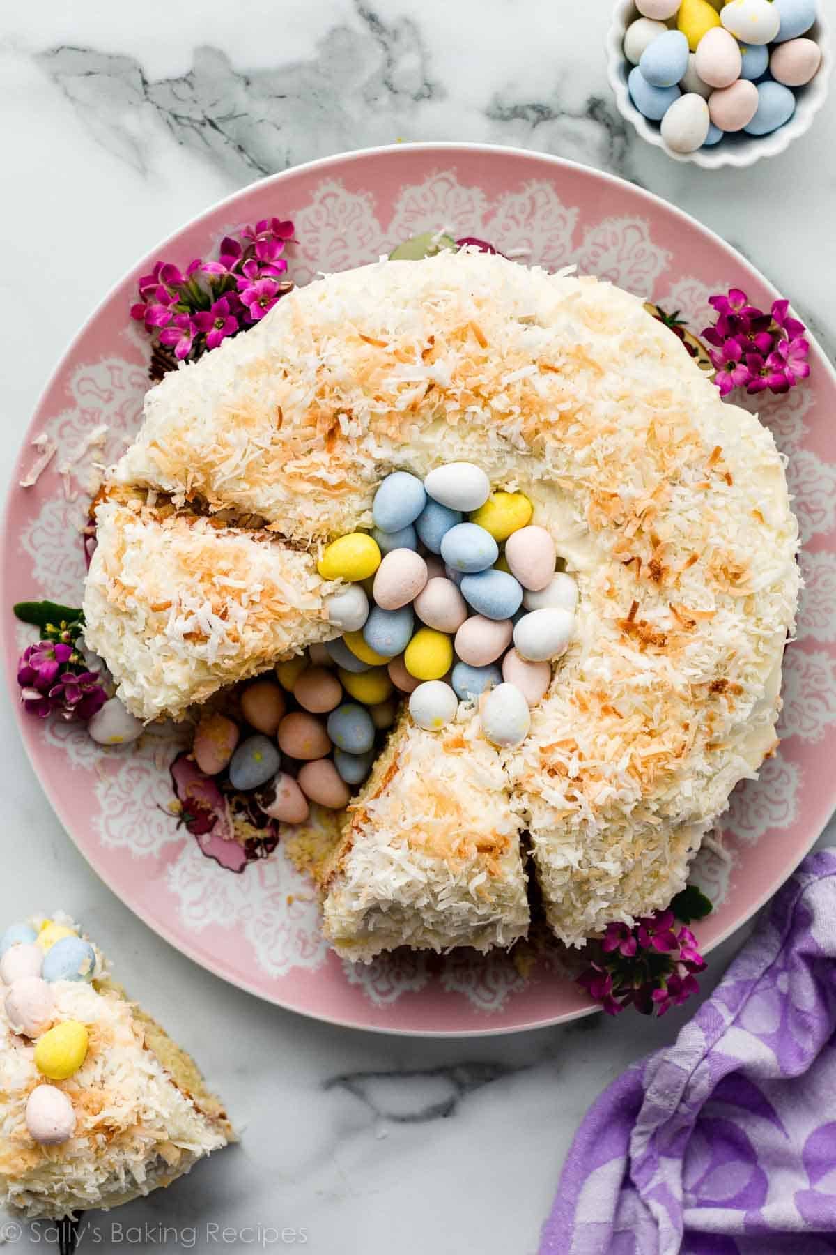 Easter cake decorated like a nest with a Bundt cake, coconut, and Easter chocolate egg candies on pink serving dish.